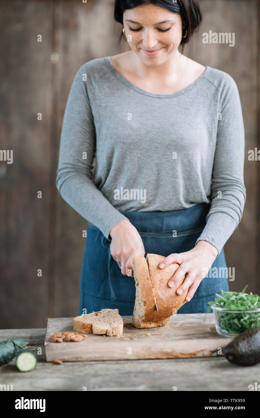 Donna pane di taglio su un tavolo di legno a casa Foto Stock