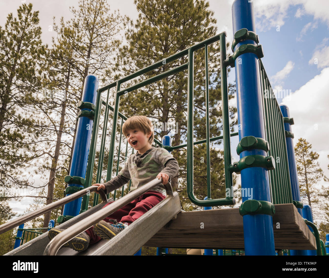 Basso angolo vista di felice ragazzo scivolare su slitta contro il cielo al parco giochi Foto Stock