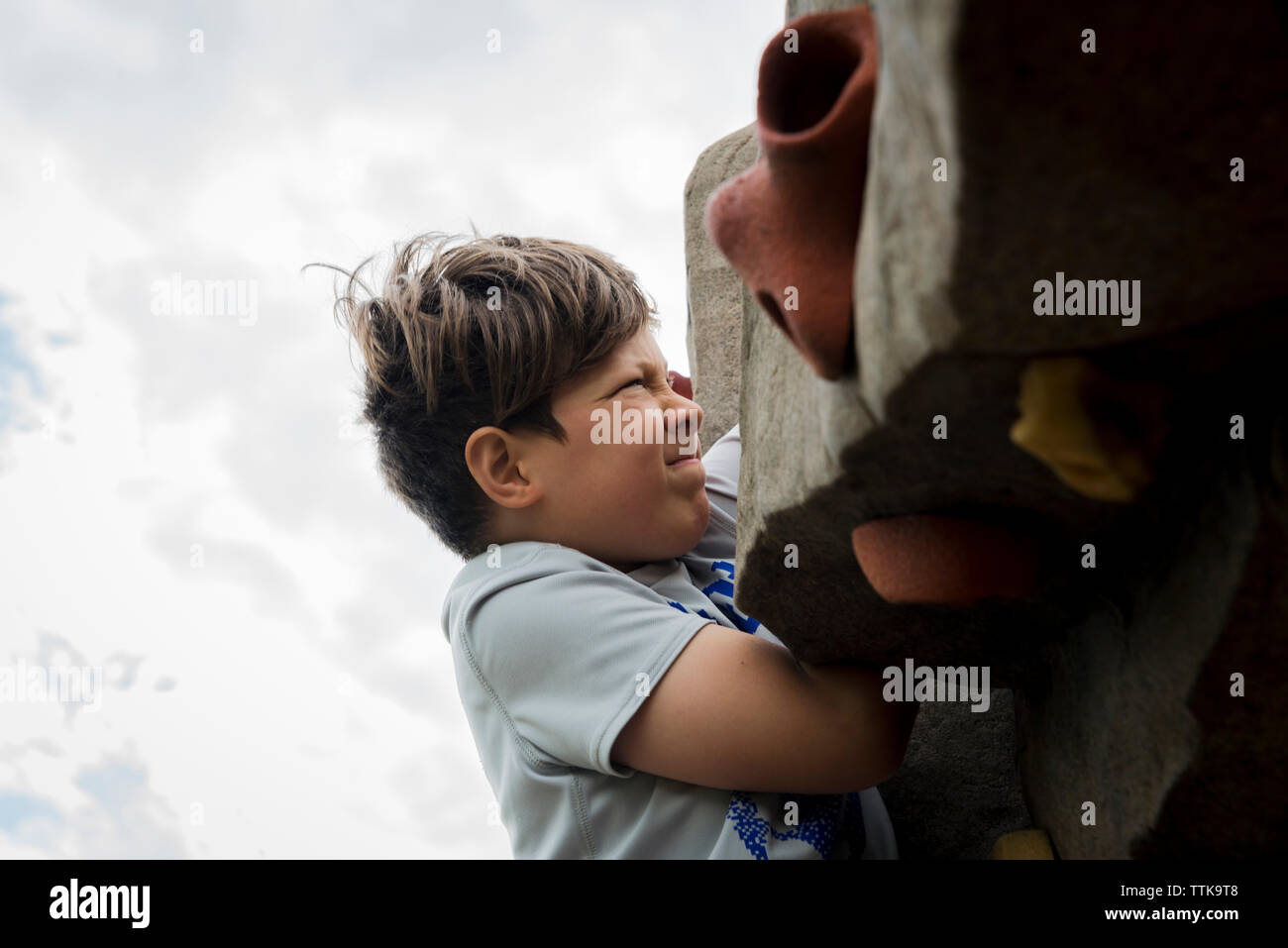 Basso angolo vista del ragazzo arrampicata su roccia contro il cielo nuvoloso al parco giochi Foto Stock