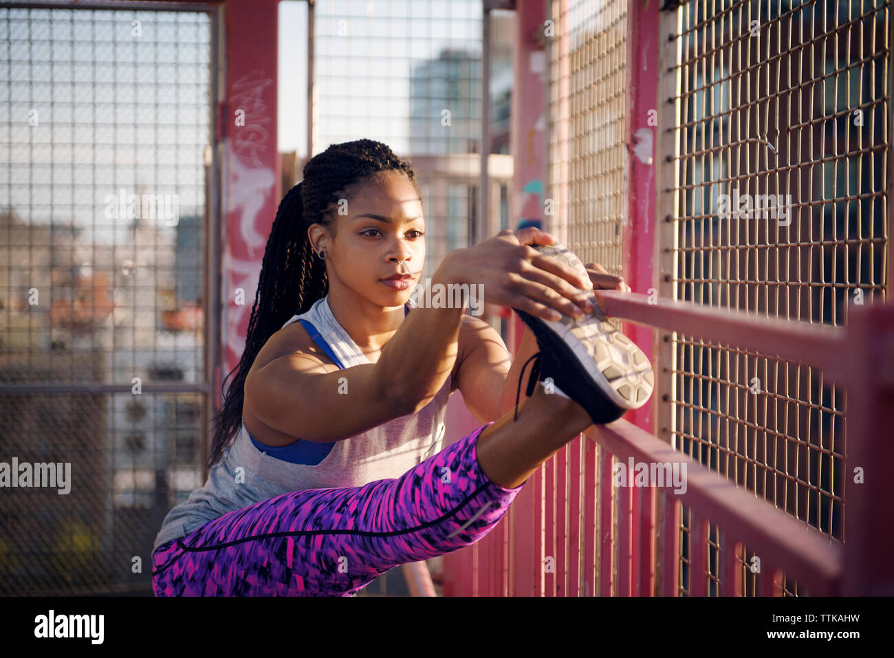 Sportive stretching mentre esercita sulla recinzione rosa Foto Stock