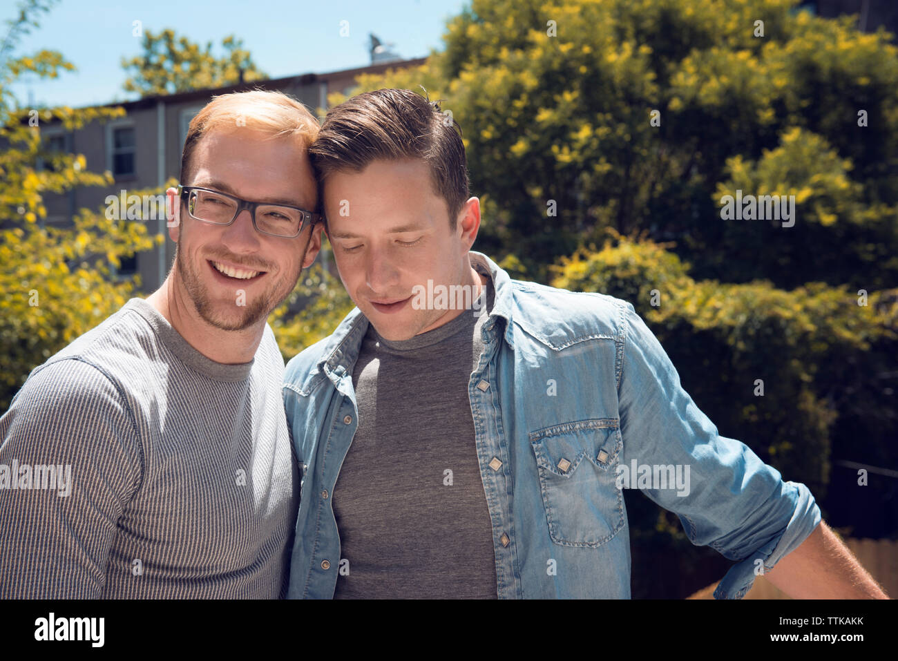 Amorevole coppia gay in piedi in balcone contro alberi Foto Stock