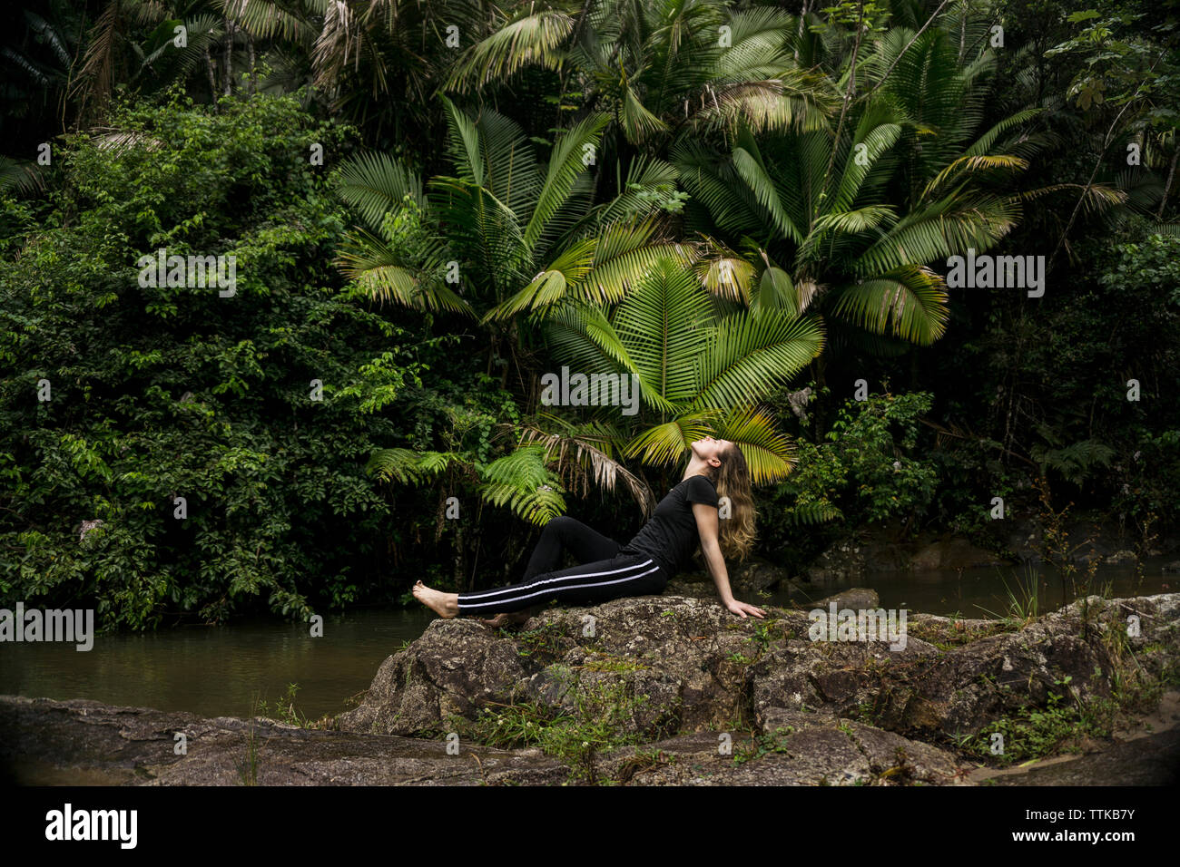 Vista laterale della donna rilassante sulle rocce sul lungolago di El Yunque National Forest Foto Stock