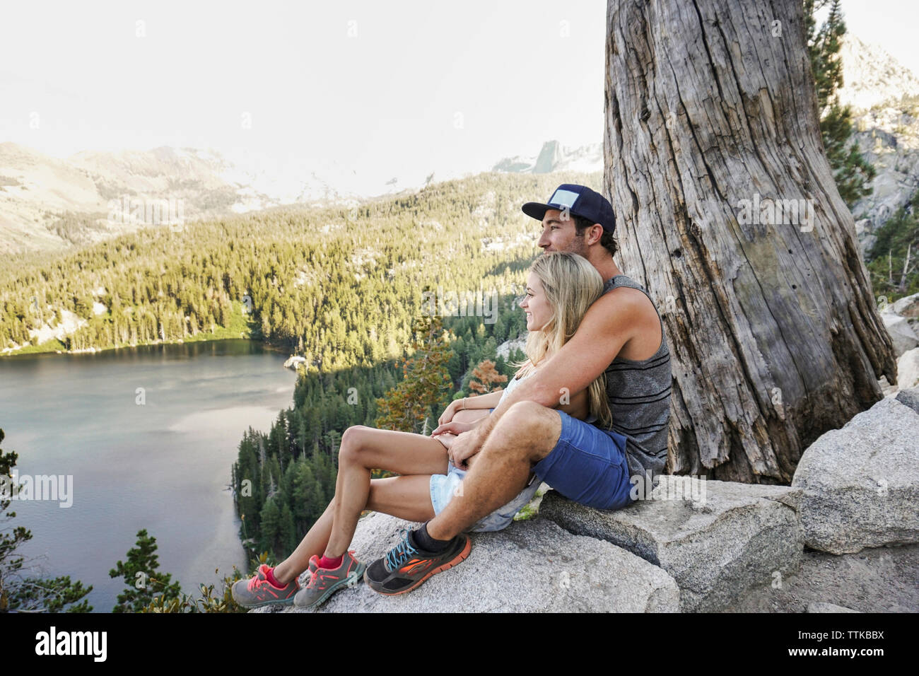 Vista laterale della coppia romantica guardando il lago seduti sulle rocce contro il cielo in foresta Foto Stock