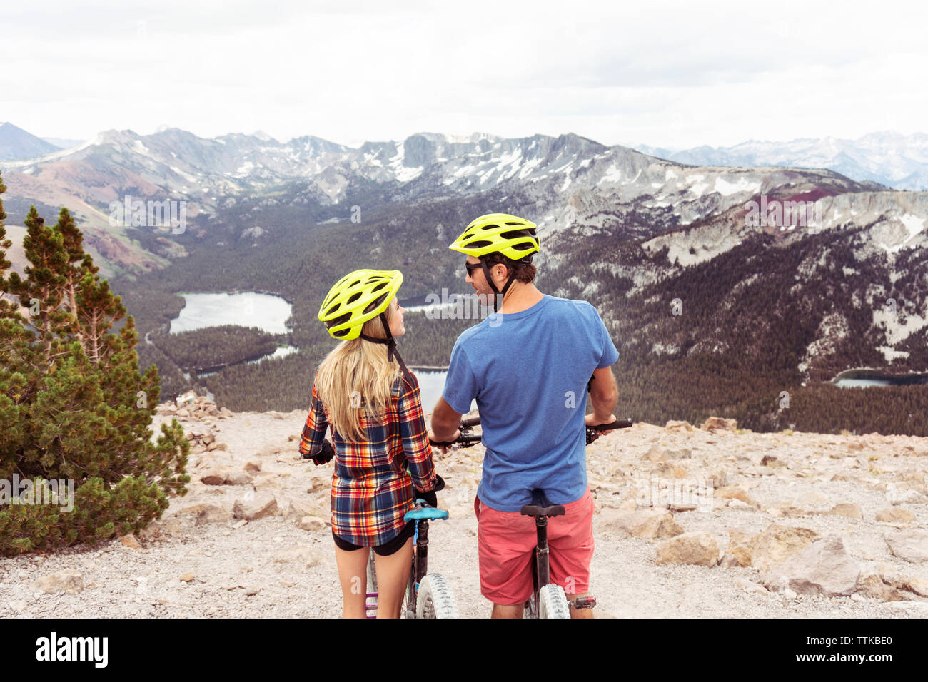 Vista posteriore della coppia romantica con le biciclette guardando ogni altra mentre si sta in piedi sul monte contro il cielo nuvoloso Foto Stock