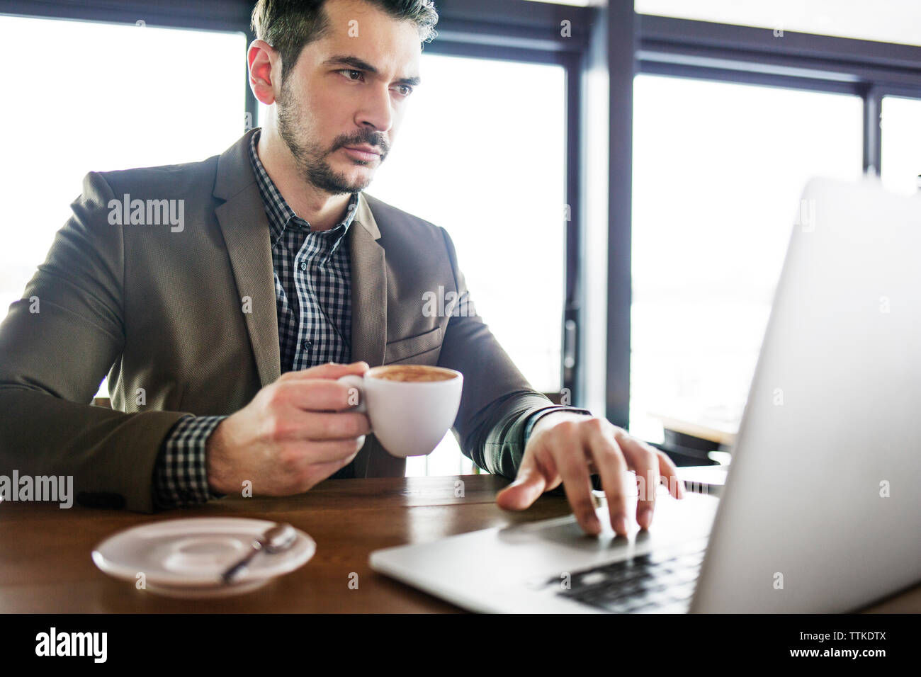Imprenditore concentrato holding tazza di caffè mentre si lavora sul computer portatile in cafe Foto Stock