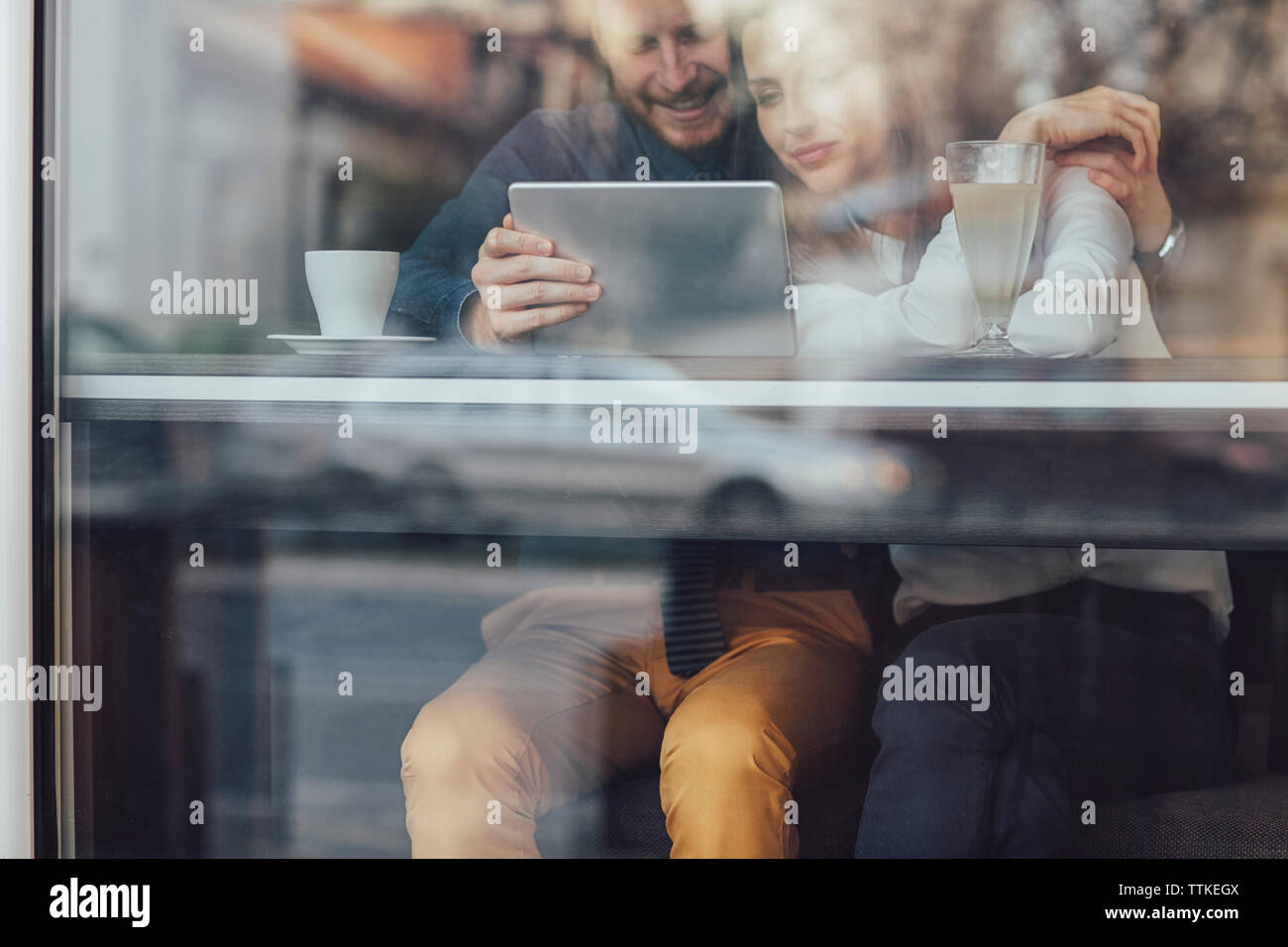 Affettuosa coppia di business utilizzando computer tablet presso il cafe visto attraverso il vetro della finestra Foto Stock