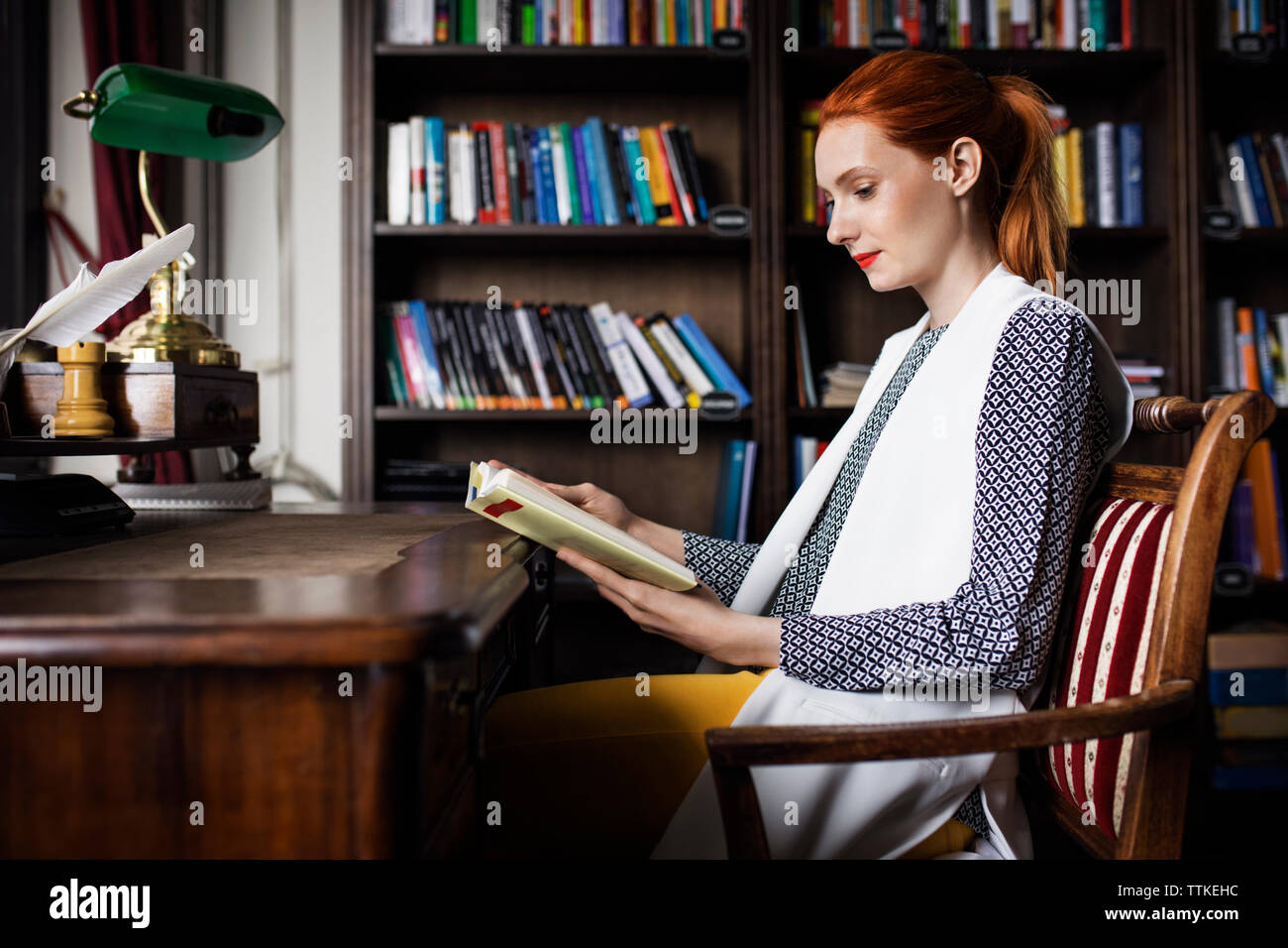 donna d'affari che legge un libro alla scrivania nell'ufficio creativo Foto Stock