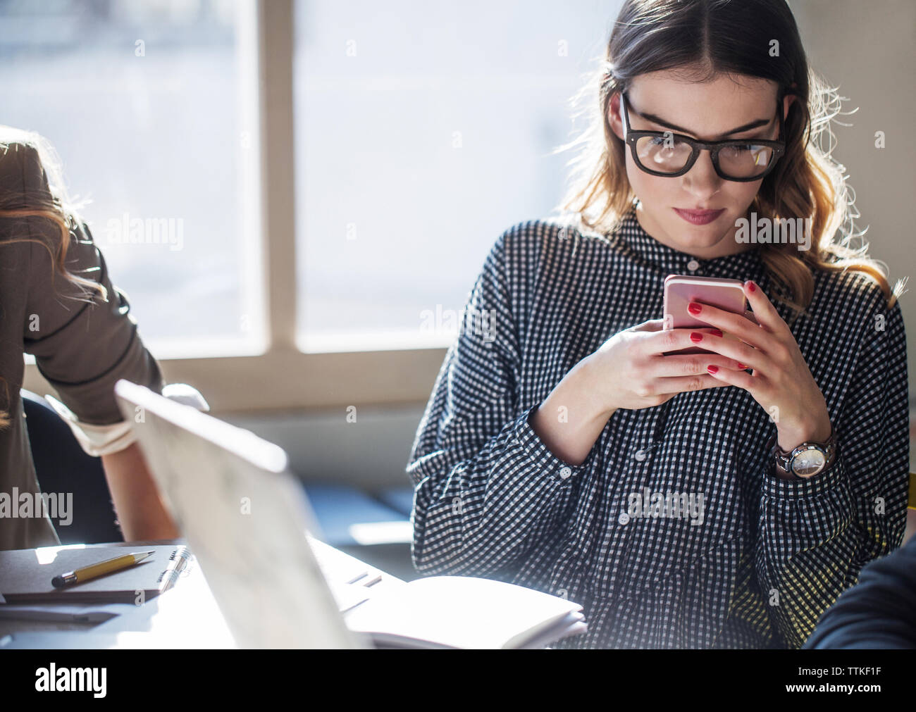 Donna che utilizza smart phone mentre è seduto a tavola in aula Foto Stock