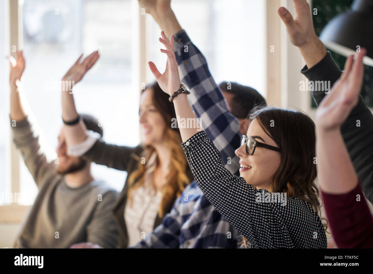 Gli studenti alzando le mani mentre è seduto a tavola in aula Foto Stock