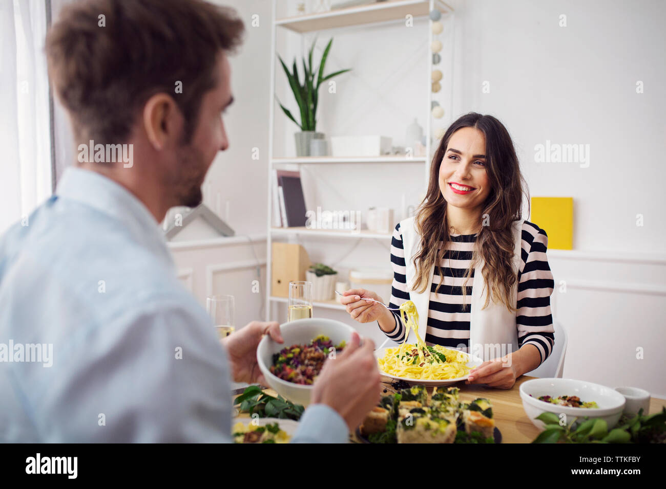 Donna felice di mangiare gli spaghetti mentre guardando amico nel partito di pranzo Foto Stock