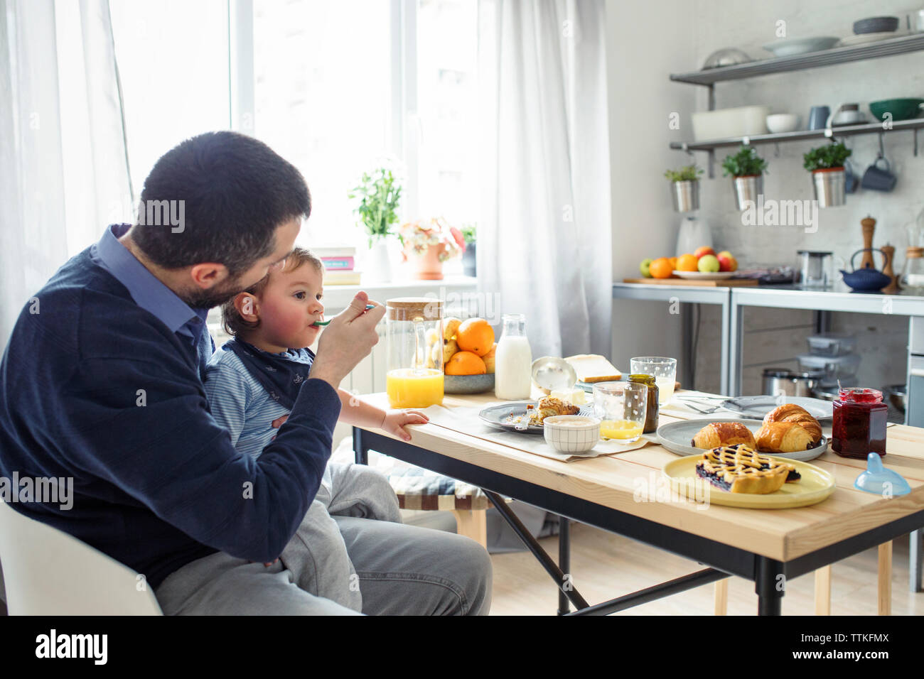 Padre alimentando la colazione al figlio a tavola in cucina Foto Stock
