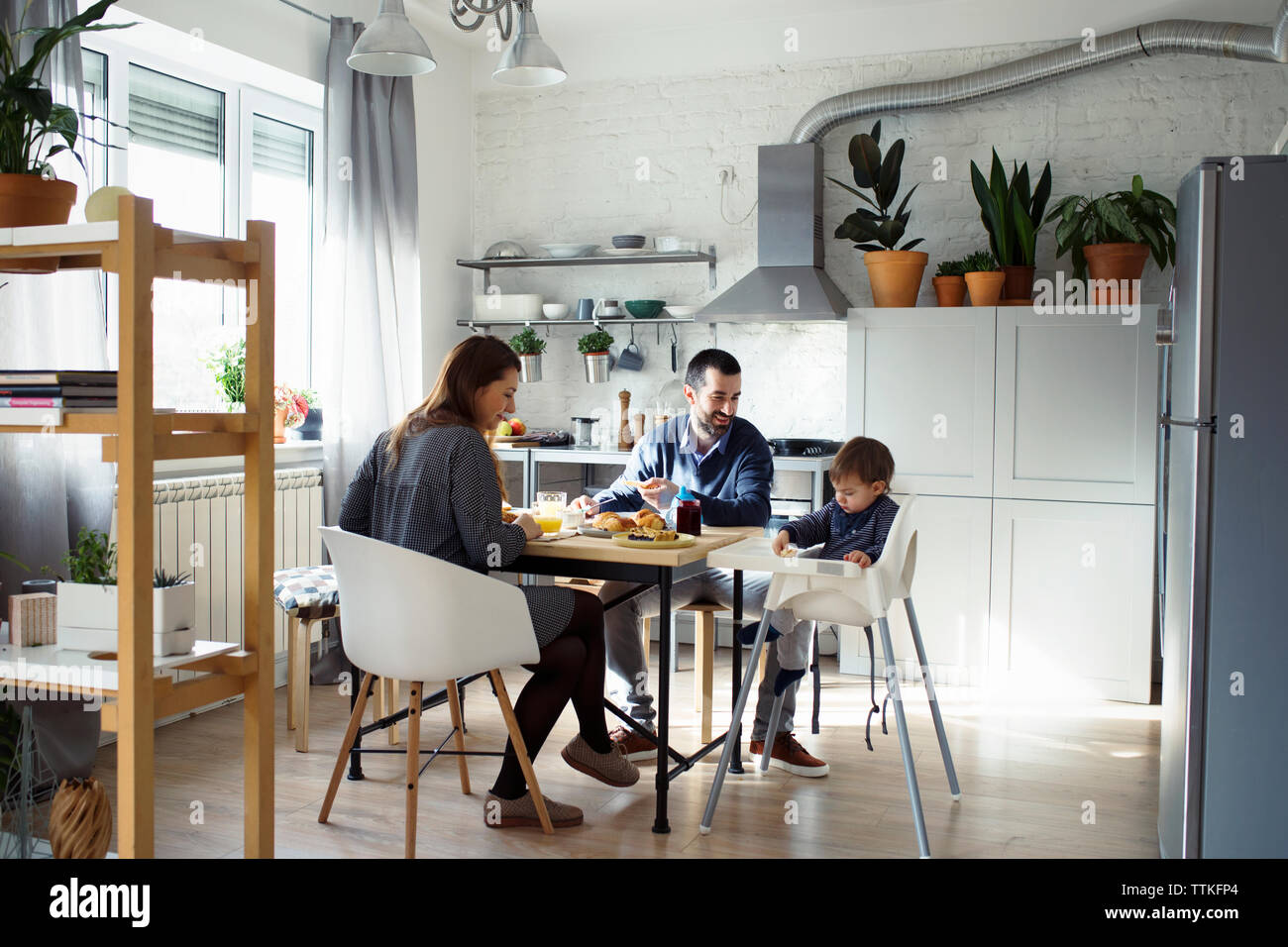 I genitori guardando il figlio seduto sulla sedia alta pur avendo prima colazione in cucina Foto Stock