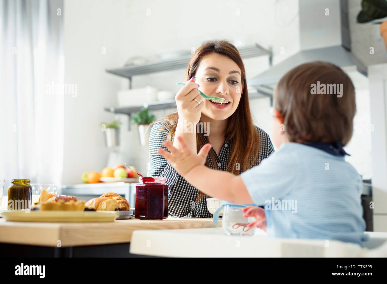 Alimentazione madre prima colazione al figlio a tavola in cucina Foto Stock
