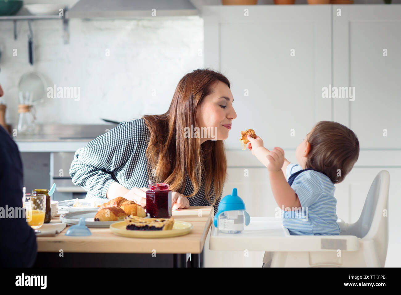 Uomo che guarda un figlio di madre di alimentazione a tavola in cucina Foto Stock