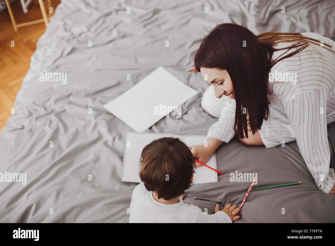 Angolo di alta vista di felice la madre e il bambino con forniture scolastiche su letto di casa Foto Stock