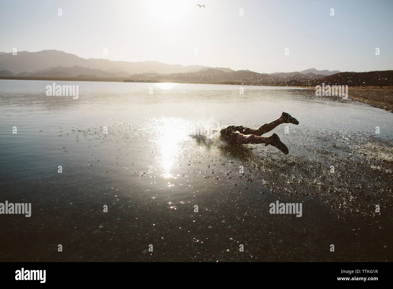 Carefree uomo saltando nel lago contro il cielo chiaro durante la giornata di sole Foto Stock