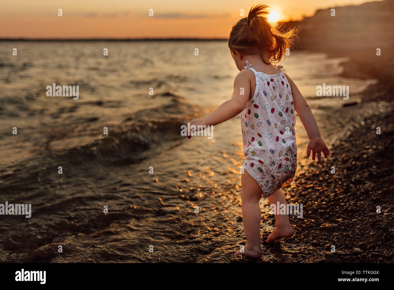 Per tutta la lunghezza della bambina in piedi sulla riva durante il tramonto Foto Stock