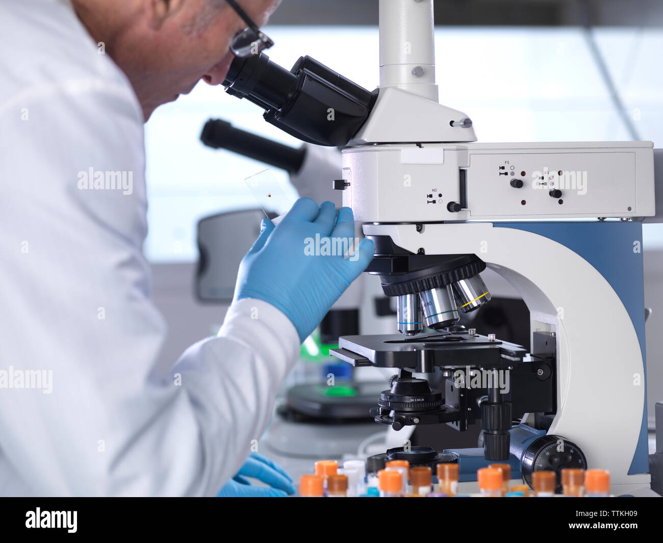 Vista laterale dello scienziato analizzando i campioni di sangue attraverso il microscopio in laboratorio Foto Stock