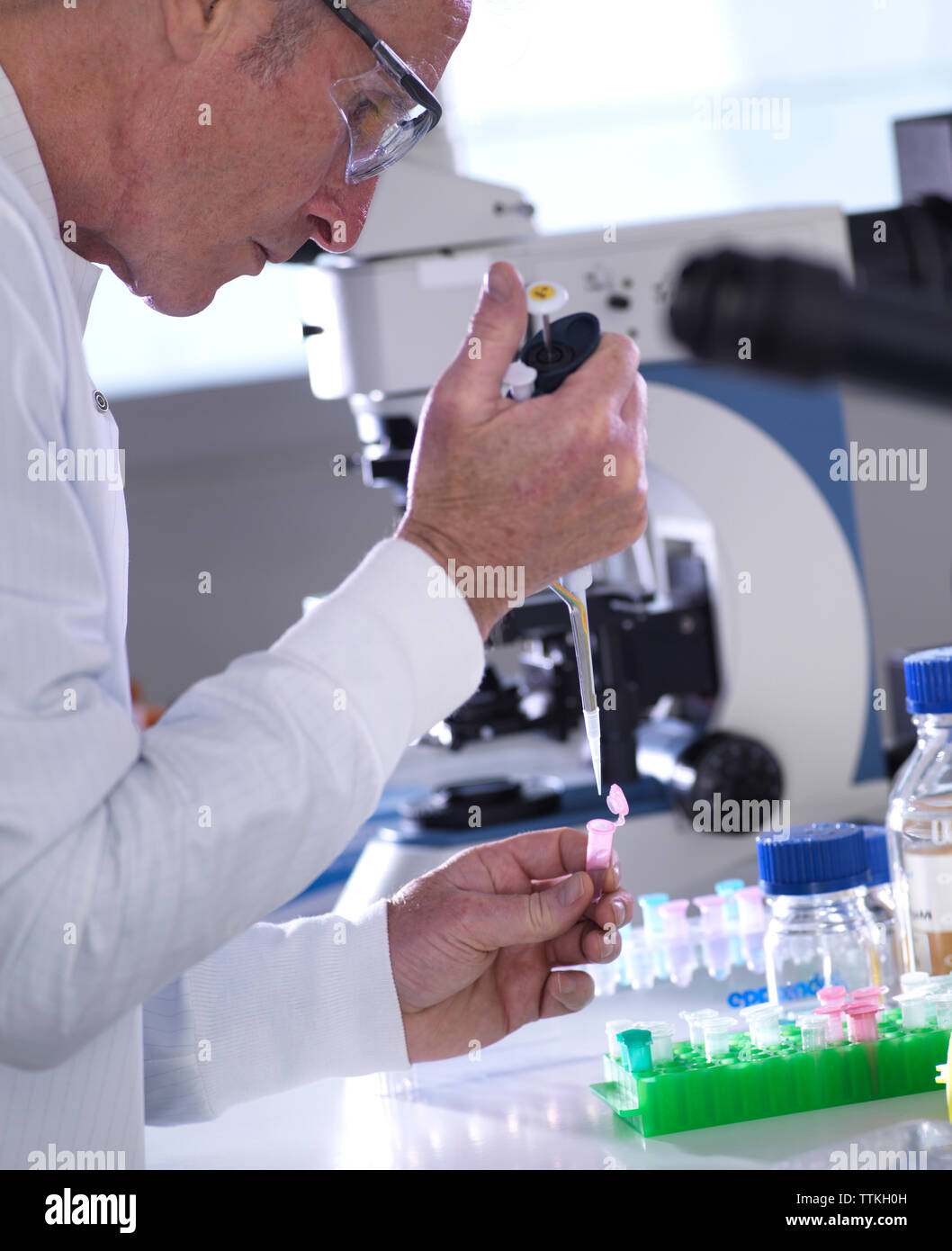 Vista laterale di uno scienziato maschio il pipettaggio di campioni in flaconcino sulla tabella in laboratorio Foto Stock