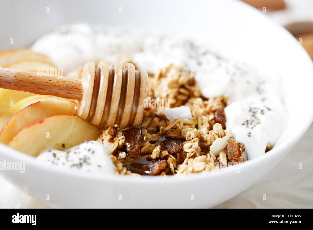 Close-up di miele il bilanciere con fette di mela e yogurt in cereali per la prima colazione sul tavolo Foto Stock
