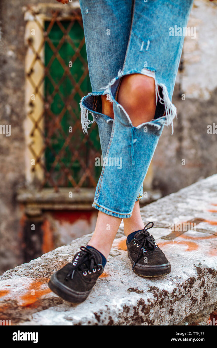 Sezione bassa della donna che indossa jeans strappati mentre in piedi sulla parete di ritegno Foto Stock