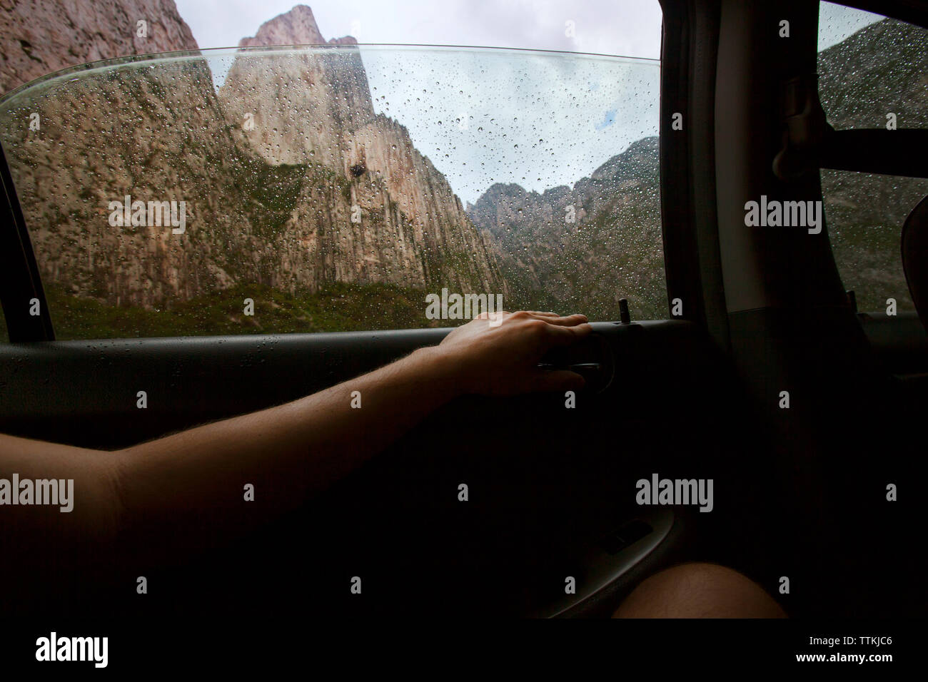 Immagine ritagliata della persona seduta in auto con le montagne sullo sfondo Foto Stock
