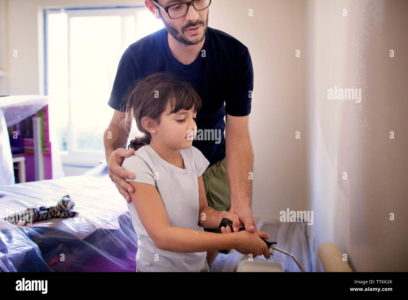 Padre ad assistere la figlia in pittura la parete di casa Foto Stock