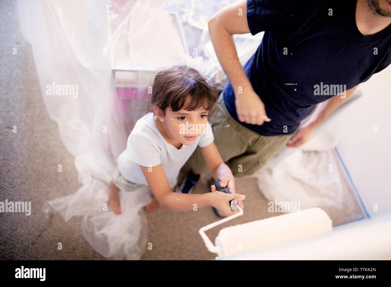 Ragazza in piedi oltre al padre mentre la pittura parete di casa Foto Stock