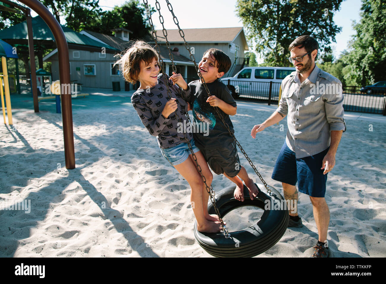 Padre guardando i bambini che giocano su tire swing in cortile Foto Stock