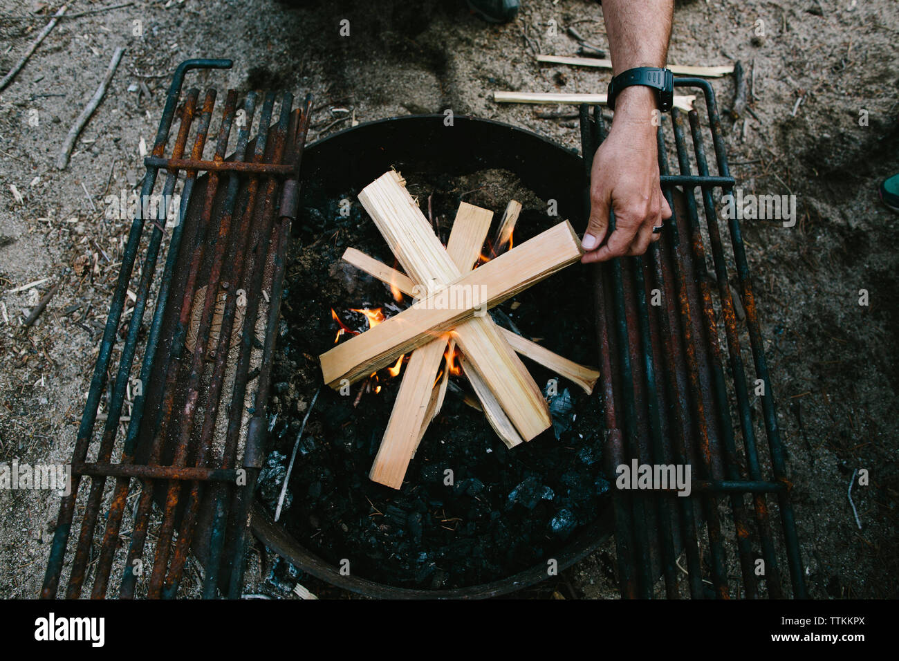 Elevato angolo di visione dell uomo la combustione di legna da ardere in una buca per il fuoco nel campeggio Foto Stock