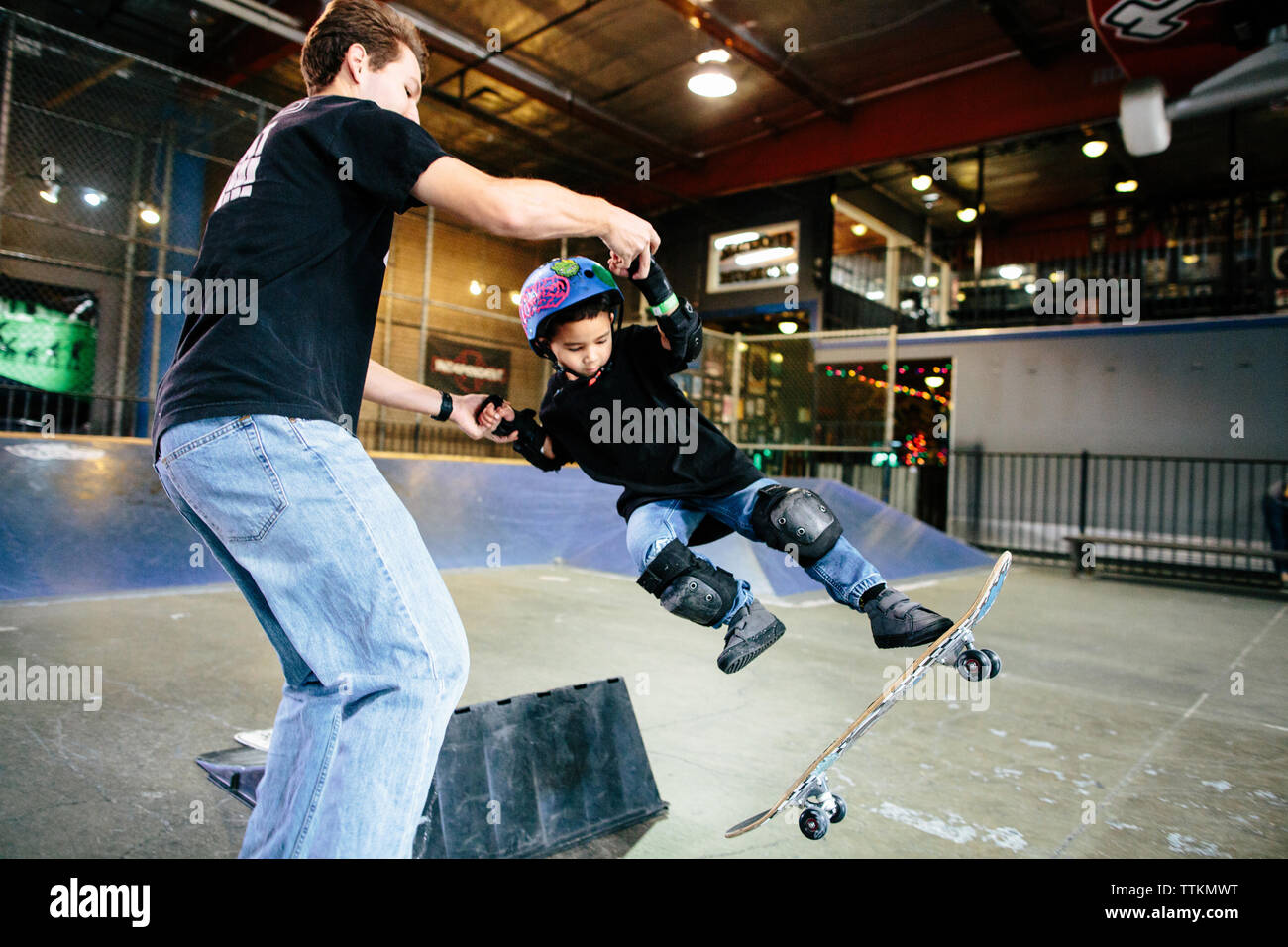 Pattinatore ragazzo perde il suo skateboard dopo un salto mentre insegnante tiene per mano Foto Stock