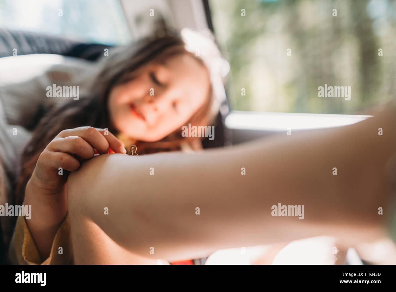 Ragazza che gioca con inchworm sul ginocchio mentre è seduto in auto Foto Stock