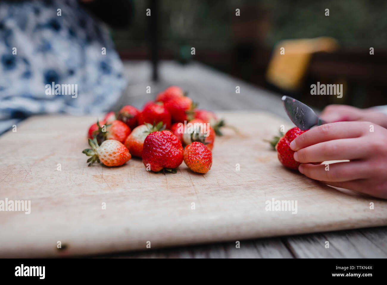 Tagliate le mani della ragazza di fragole di taglio sul bordo di taglio a tavola Foto Stock