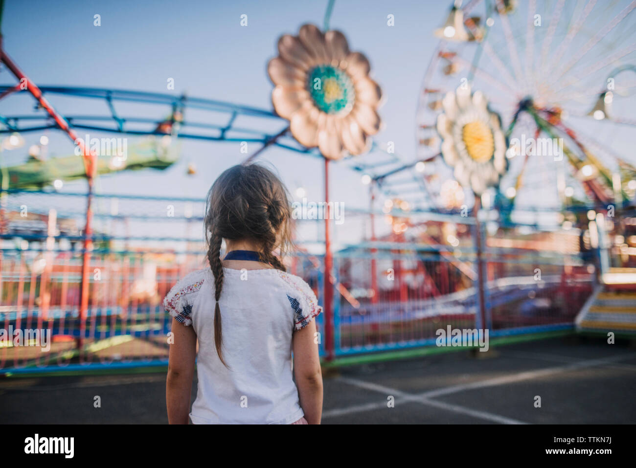 Vista posteriore della ragazza con pig-tail guardando il parco dei divertimenti di corse Foto Stock