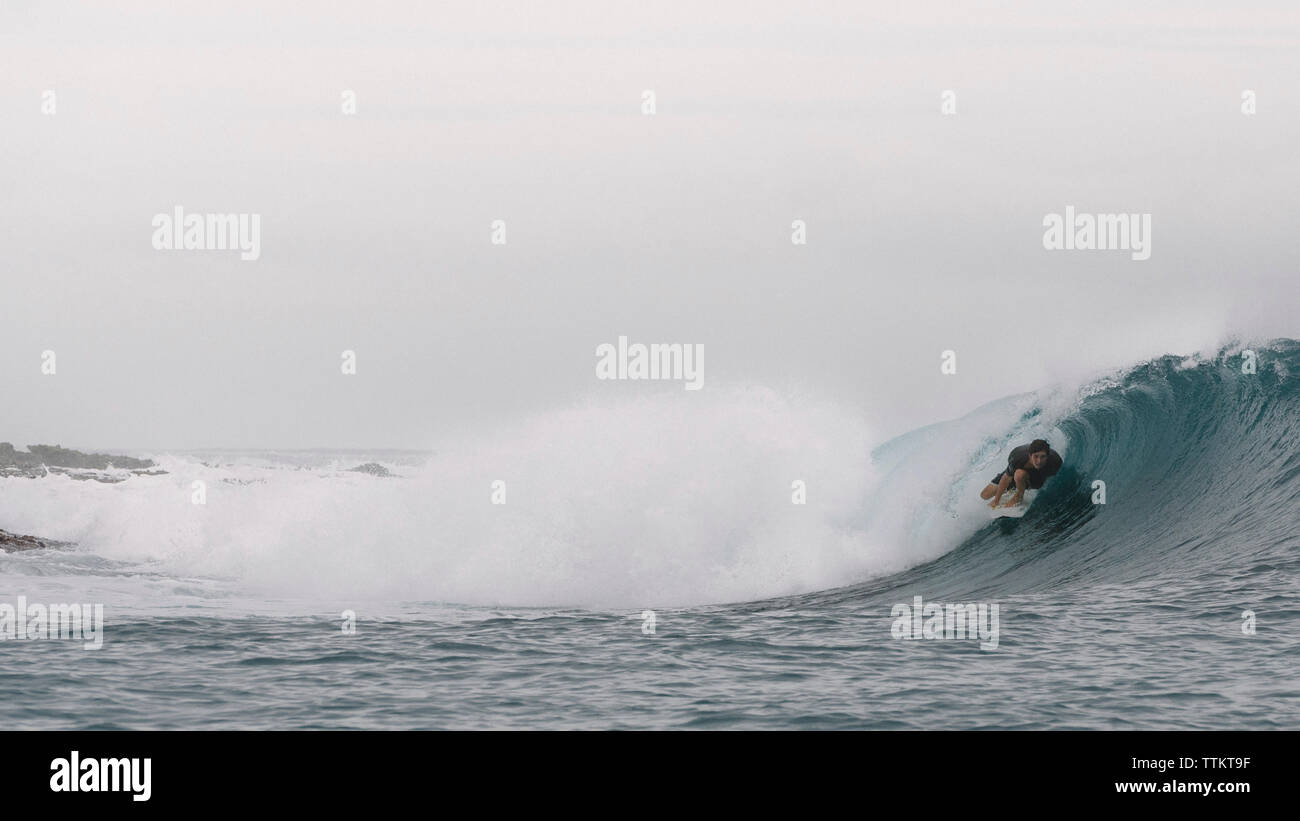 Spensierato giovane uomo surf sulla laminazione di navigare in mare contro sky Foto Stock