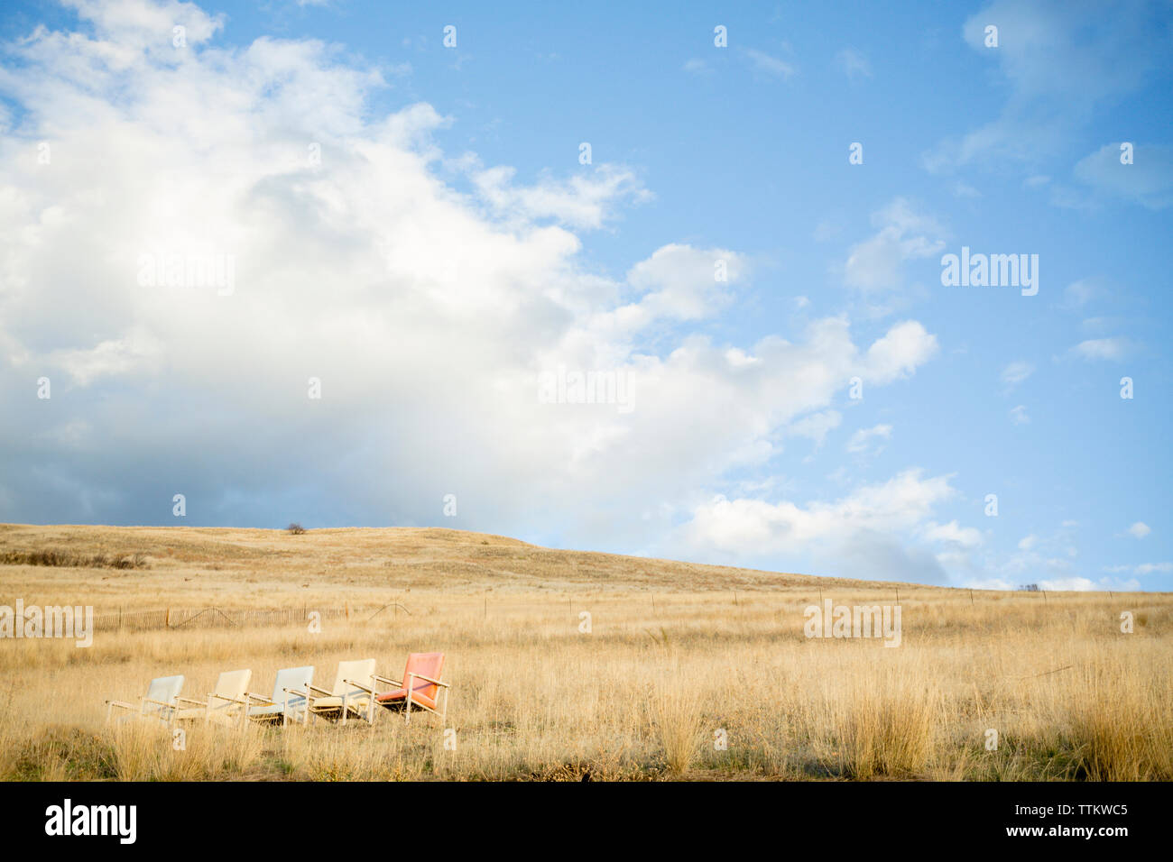 Colorate sedie vuote sul campo erboso contro il cielo nuvoloso durante la giornata di sole Foto Stock