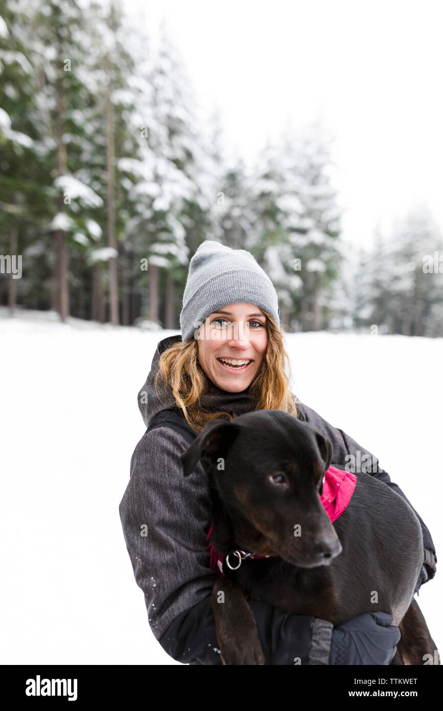 Donna sorridente holding cane nella foresta Foto Stock