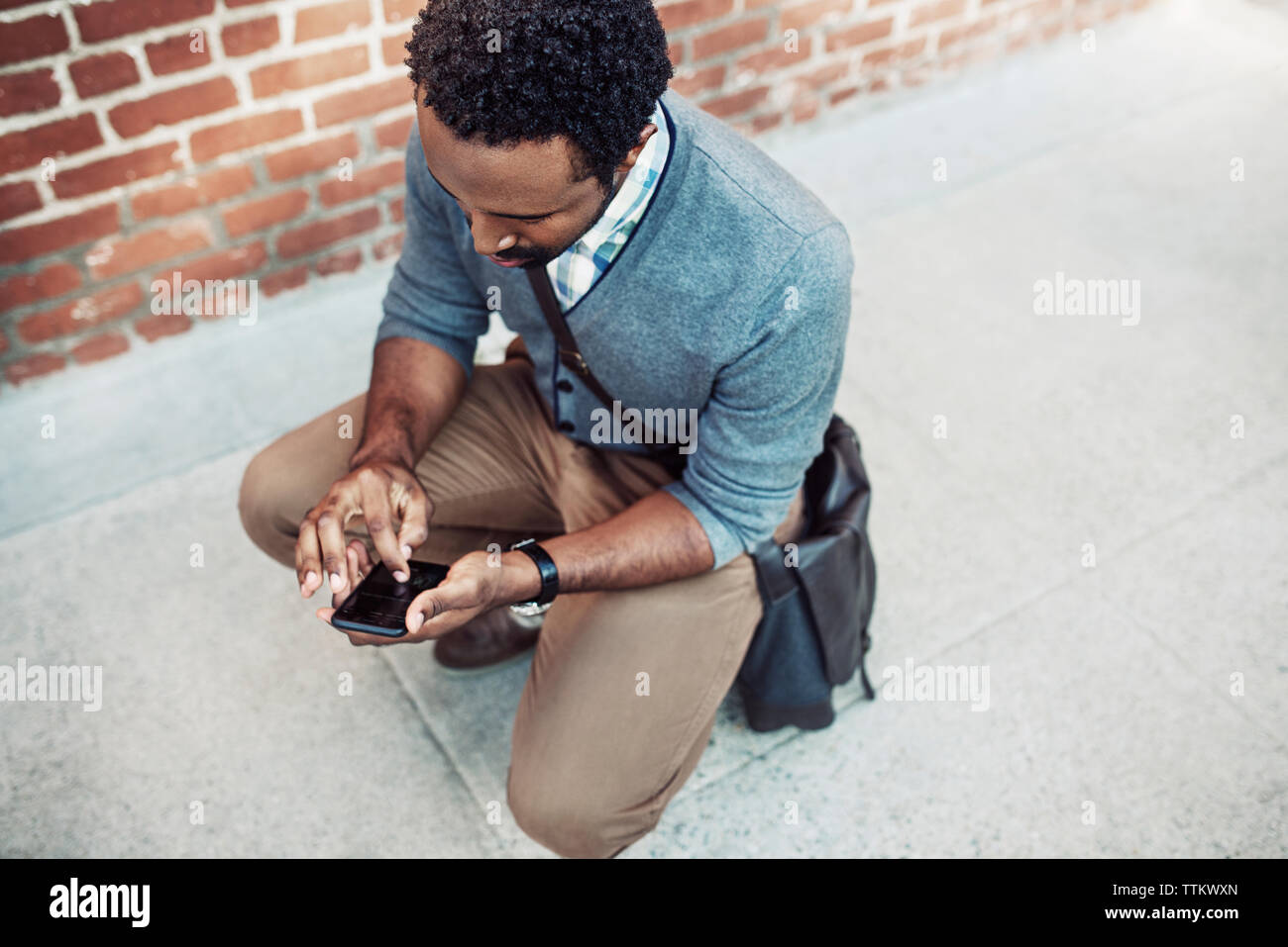 Vista aerea dell'uomo per la messaggistica di testo mentre accovacciato sul marciapiede Foto Stock
