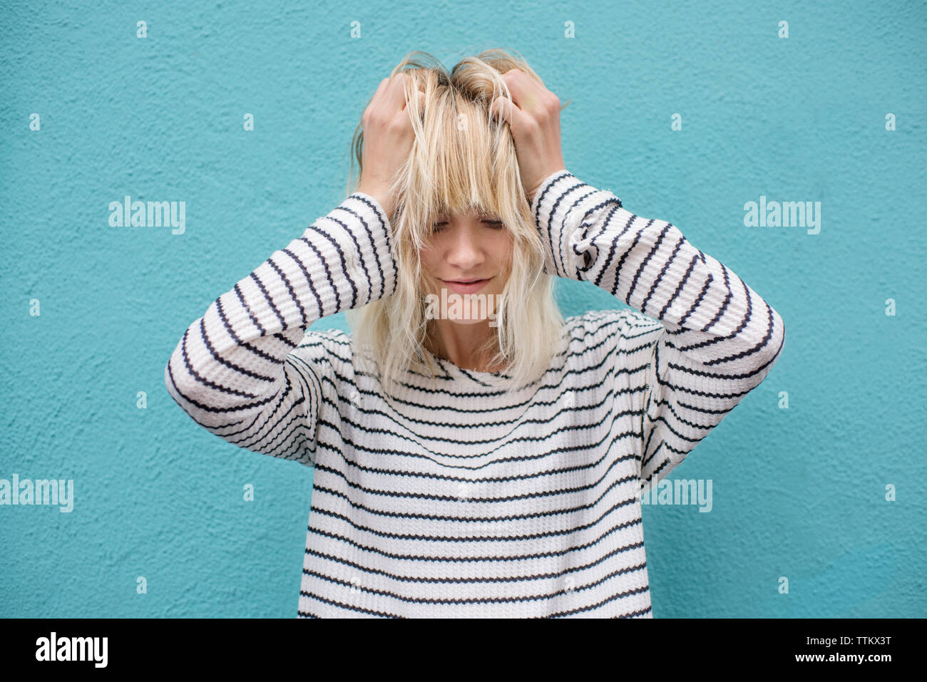 Frustrati giovane donna tira i capelli contro la parete blu Foto Stock