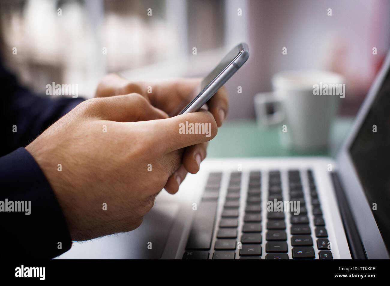 Close-up di imprenditore il mani con smart phone su computer portatile in ufficio creativo Foto Stock