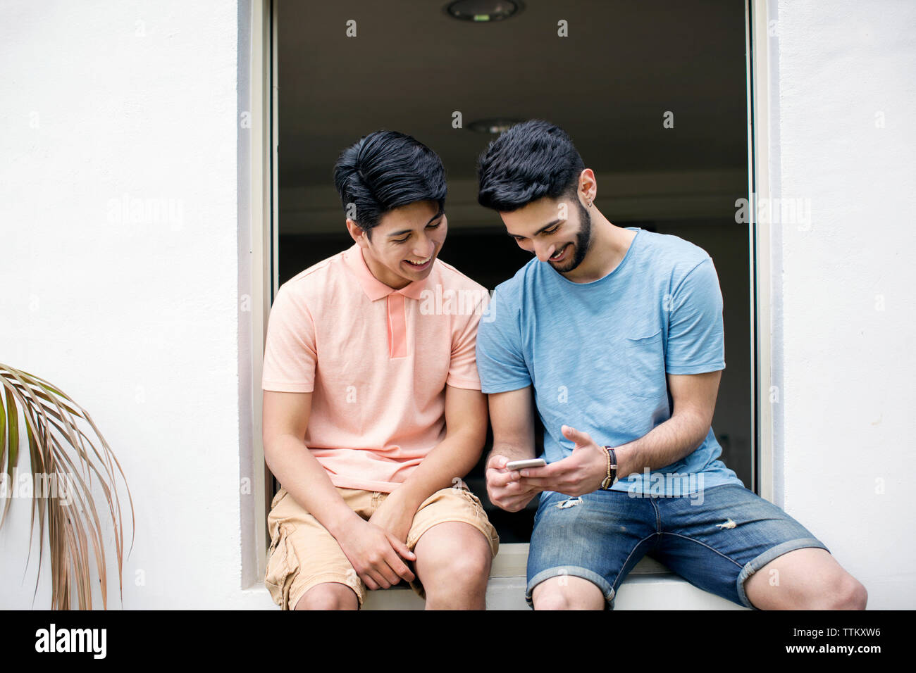 Happy amici maschio utilizzando smart phone mentre è seduto sulla finestra Foto Stock