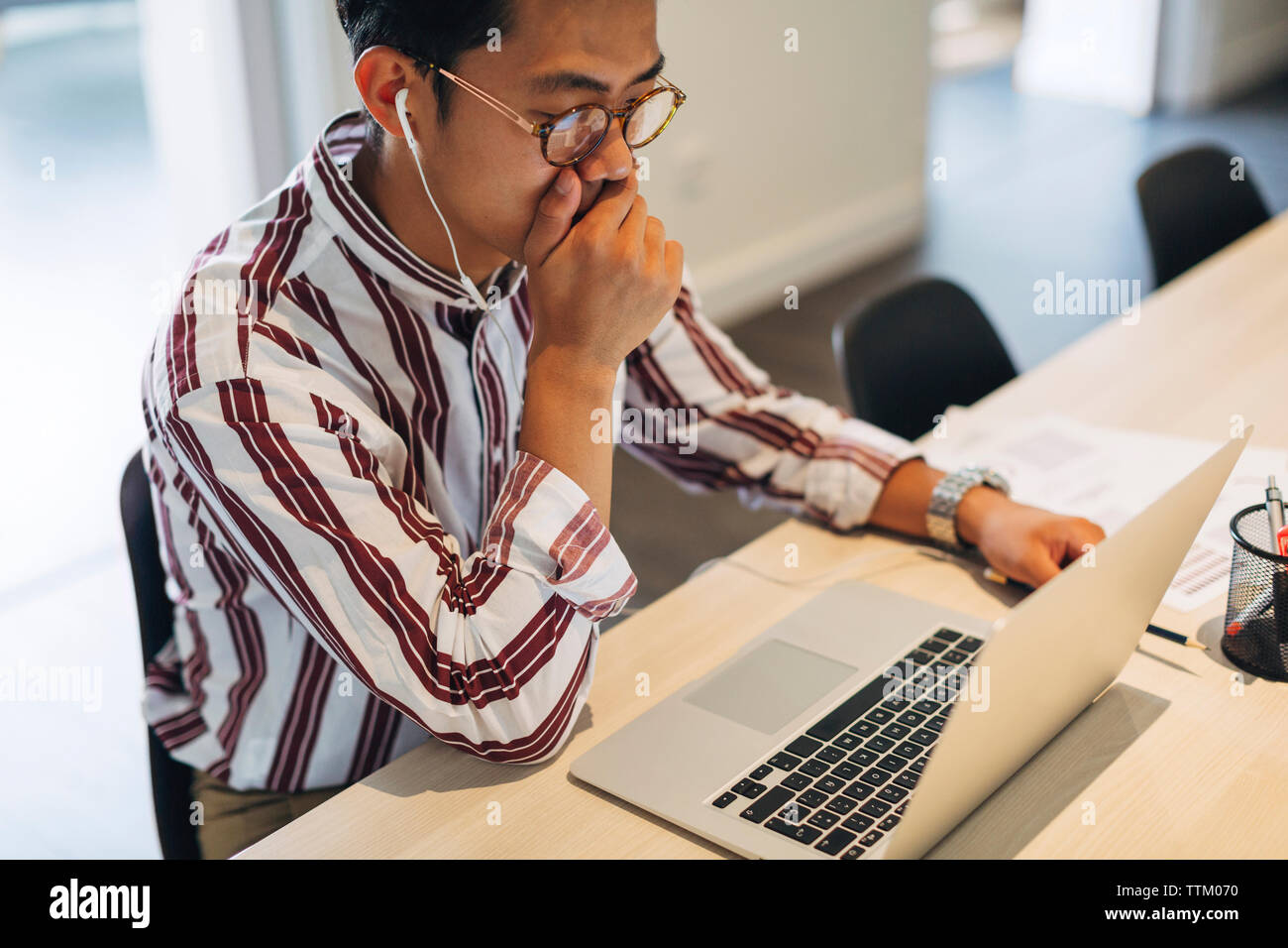Elevato angolo di visione dell uomo d affari con la mano che copre la bocca lavorando sul computer portatile in ufficio Foto Stock