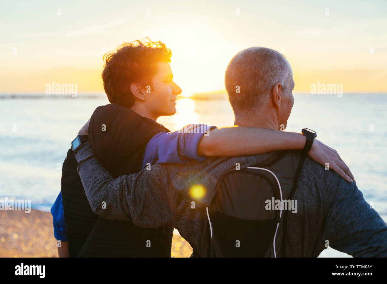 Padre e figlio con le braccia intorno alle spalle guardando a vista mentre si sta in piedi in spiaggia Foto Stock