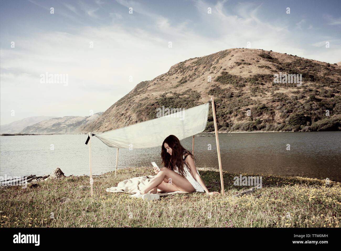 Donna di messaggistica di testo mentre seduto sotto ombra a seashore Foto Stock