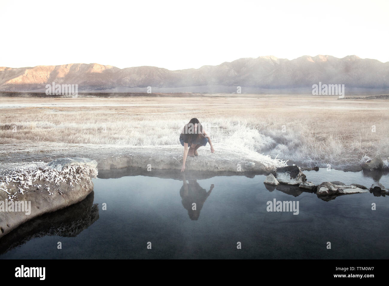 Donna di toccare acqua al lago Mammoth Hot Springs contro le montagne Foto Stock