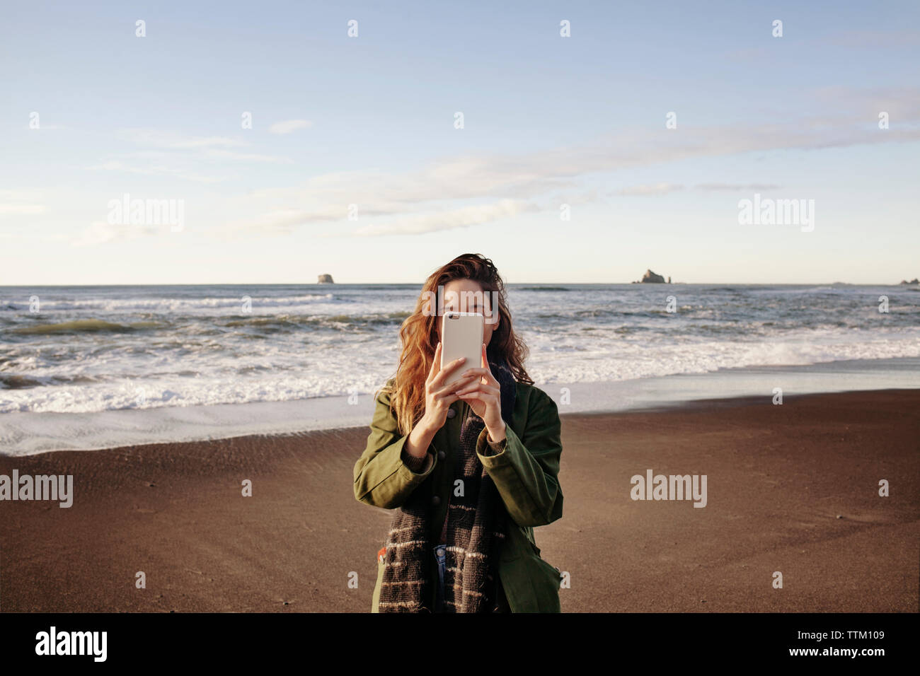 Giovane donna fotografando attraverso smart phone sulla spiaggia Foto Stock
