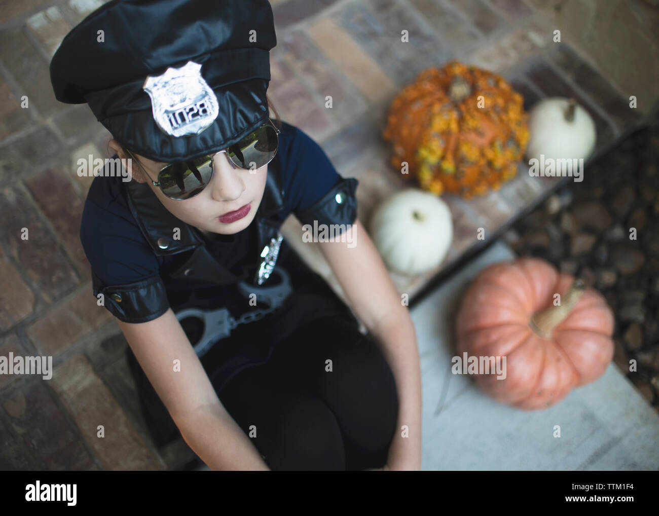 Angolo di Alta Vista della ragazza di indossare il costume di polizia e gli occhiali da sole mentre è seduto da zucche in cantiere durante il periodo di Halloween Foto Stock