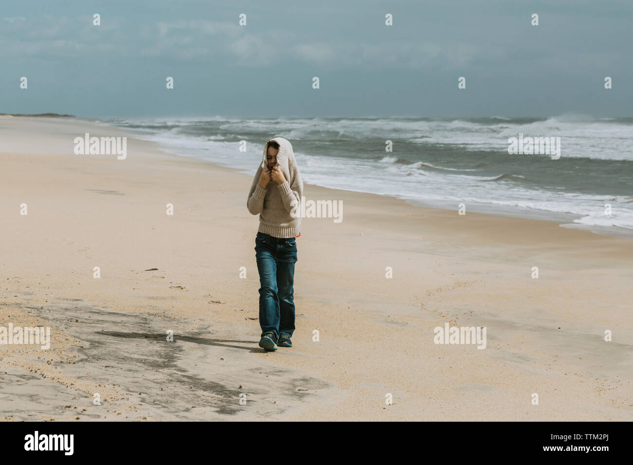 Ragazzo che copre la testa con un maglione mentre passeggiate in spiaggia contro il cielo durante la giornata di sole Foto Stock