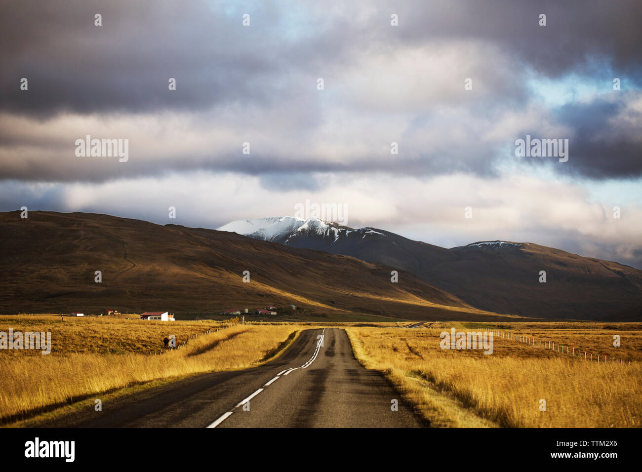 Paese strada che conduce verso le montagne contro il cielo nuvoloso Foto Stock