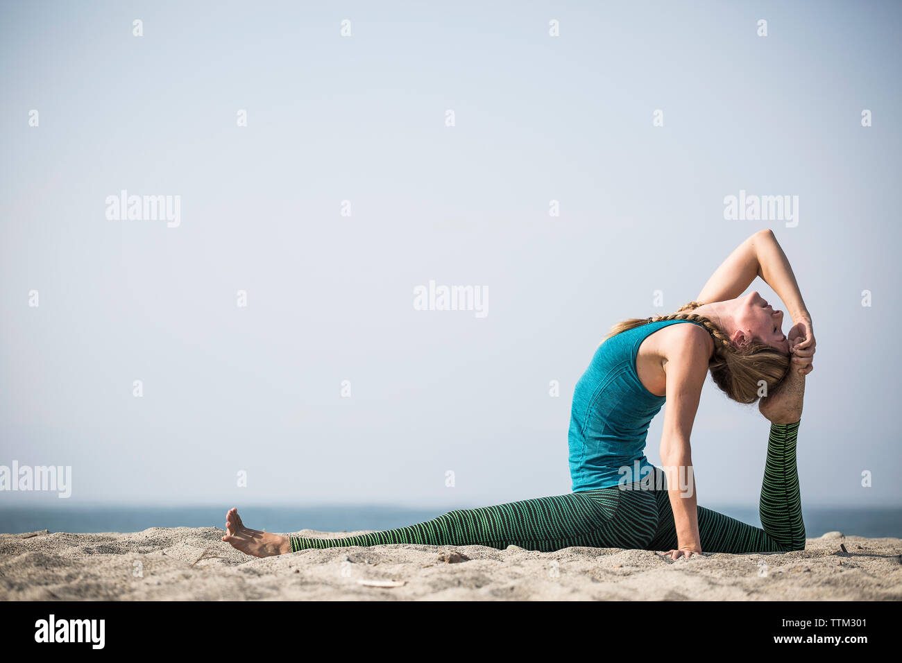 Vista laterale della donna che esercitano sulla sabbia in spiaggia contro il cielo chiaro Foto Stock